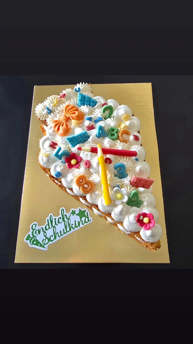Schulanfangstorte in Weiß mit ABC und Schulkind als Tortenfigur