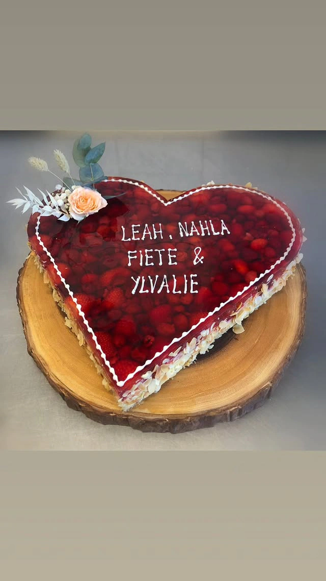 Herztorte mit roter Grütze, Creme und Blumen auf Holzbrett
