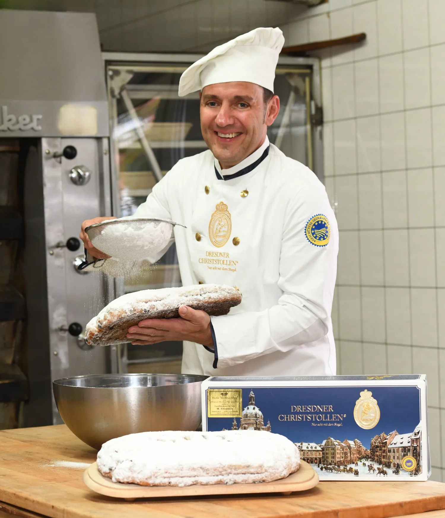 Bäckermeister Matthias Friedrich siebt Puderzucker über einen Dresdner Christstollen, daneben ein Stollenkarton mit dem Siegel des Dresdner Stollenschutzverbandes